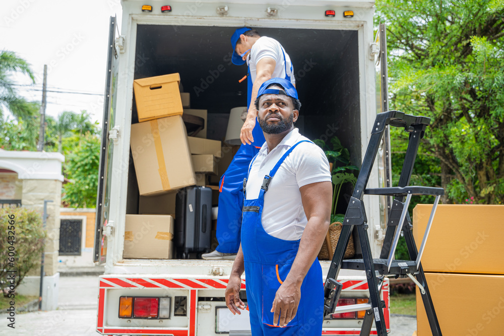 Two removal company workers are unloading boxes from a mini truck into new home.