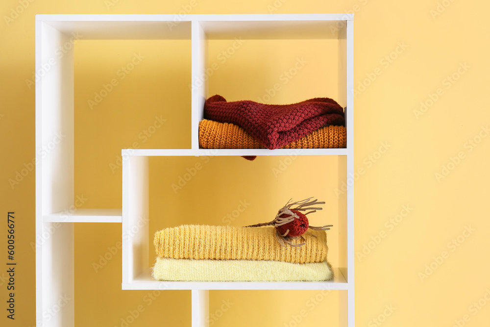 Shelf unit with beautiful sweaters and flower near beige wall in room