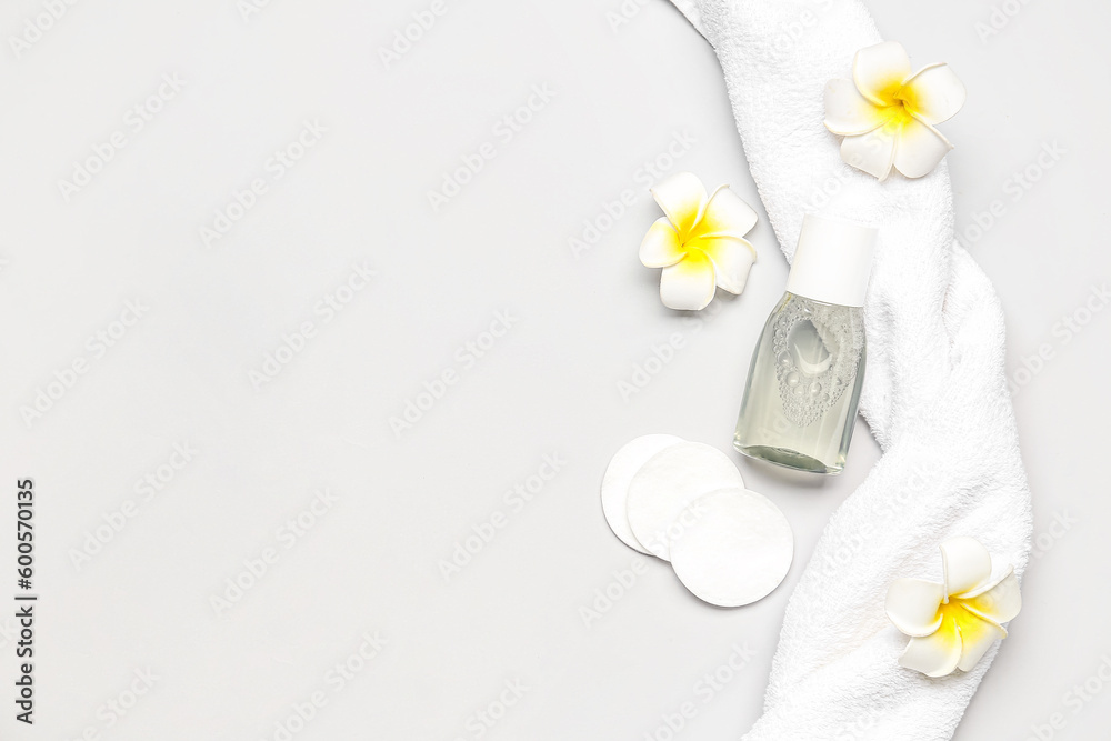 Bottle of micellar water with cotton pads, flowers and towel on light background