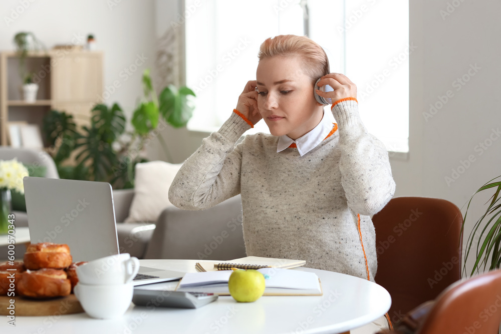 Female student in headphones studying with laptop at home