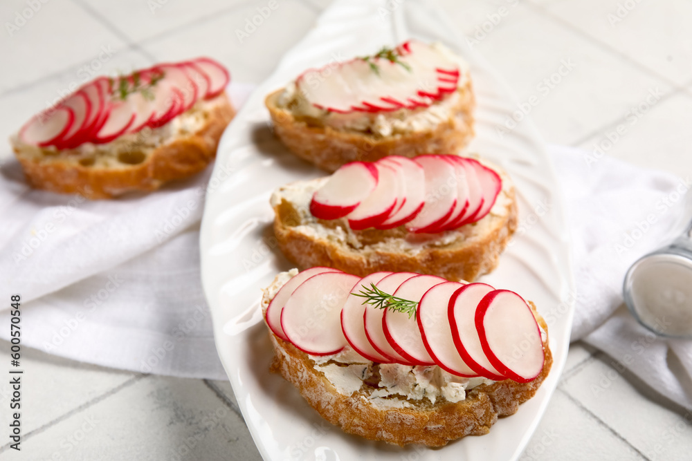 Plate with delicious radish bruschettas on white tiled table