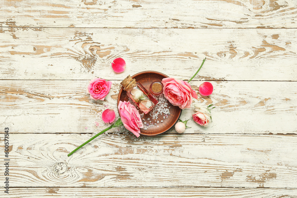 Bottles of cosmetic oil with rose extract and flowers on light wooden table