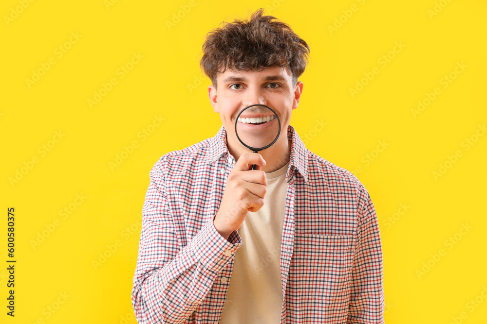 Young man with magnifier on yellow background