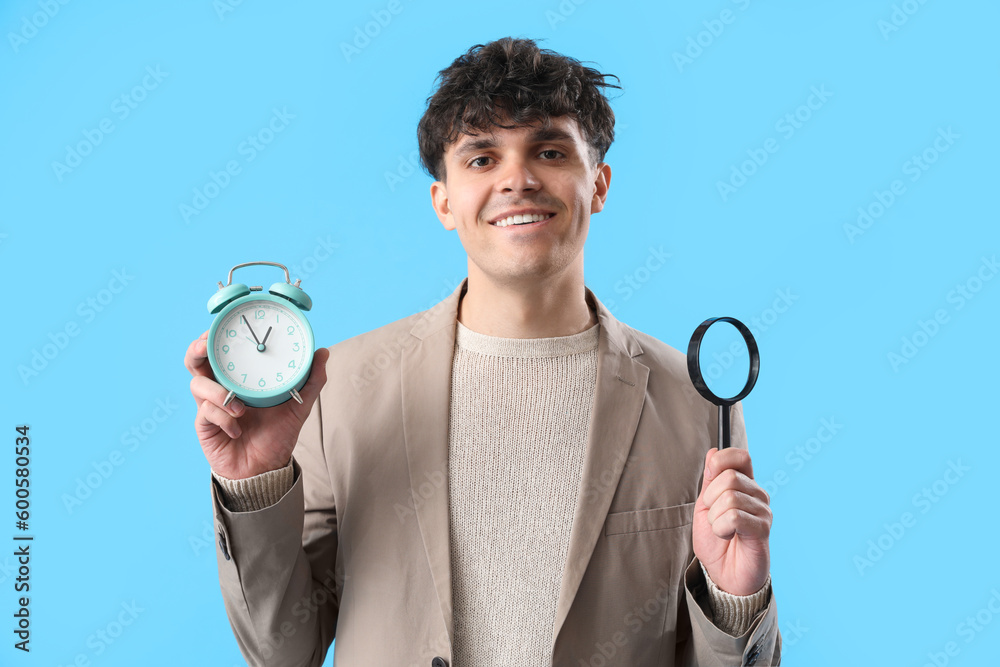 Young man with magnifier and alarm clock on blue background