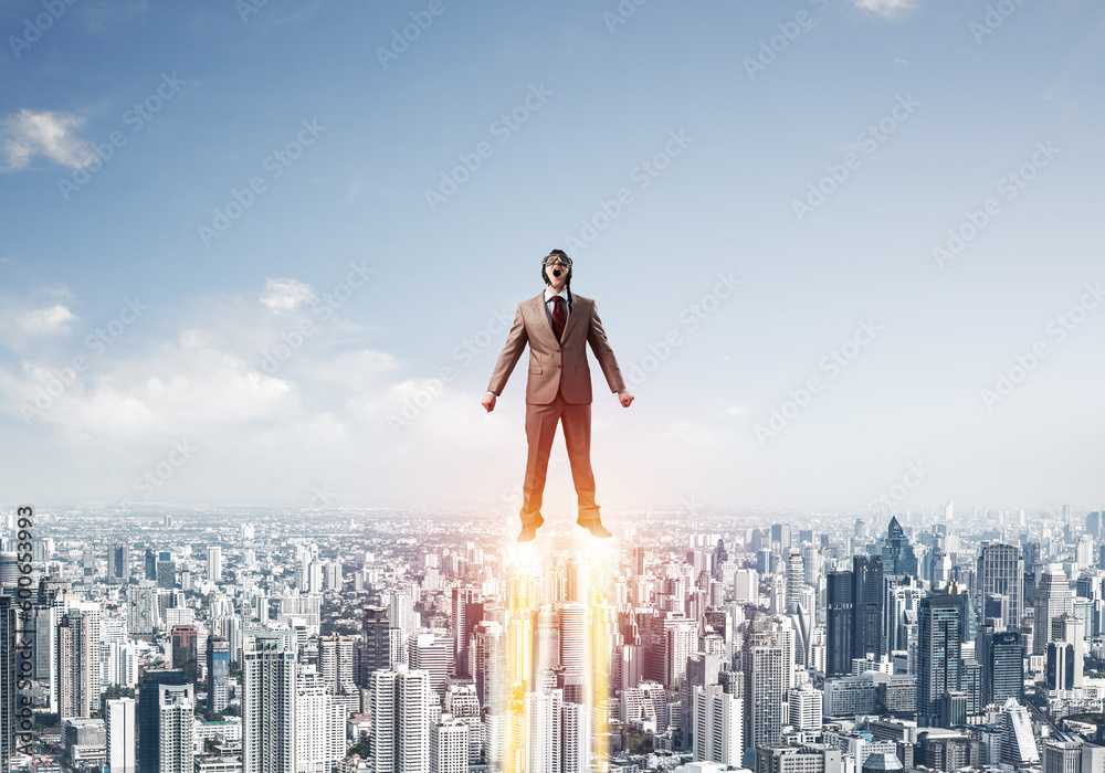 Businessman in suit and aviator hat flying in sky