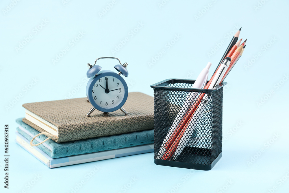 Stationery holder, notebooks and alarm on blue background