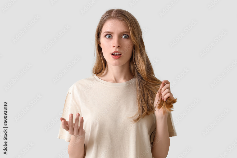 Shocked young woman with hair loss problem on light background