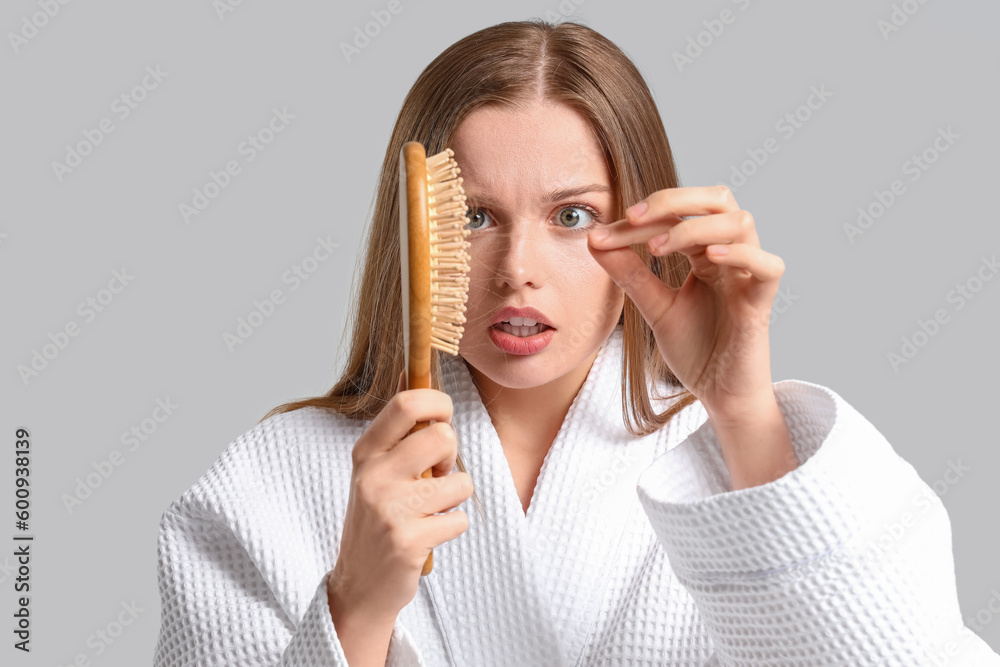 Worried young woman with hair loss problem and brush on light background