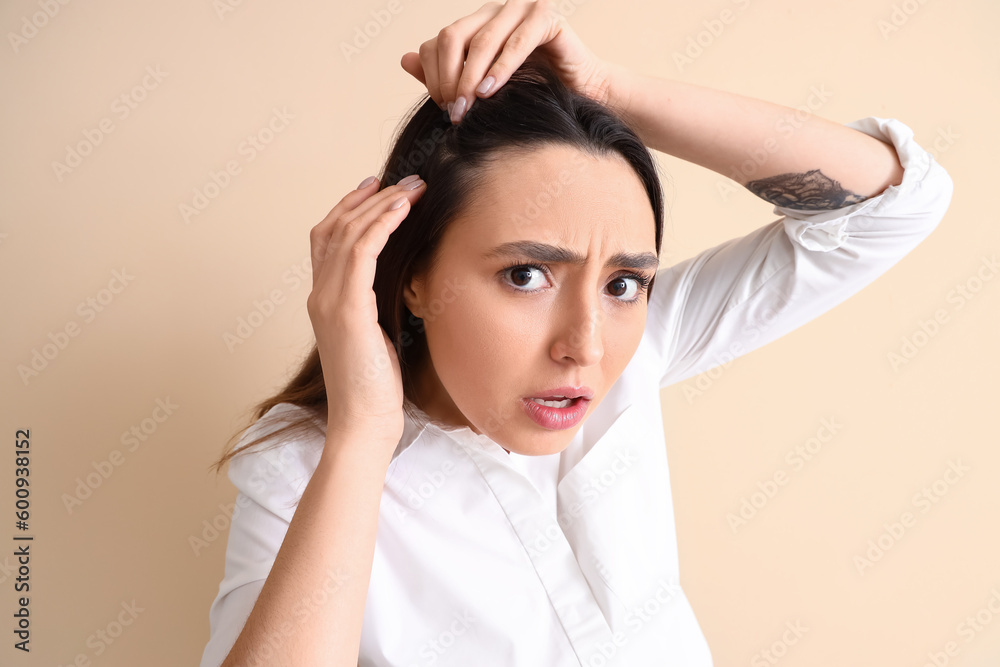 Worried young woman with hair loss problem on beige background