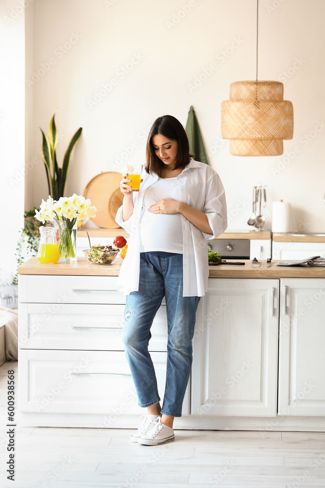 Young pregnant woman with glass of juice in kitchen