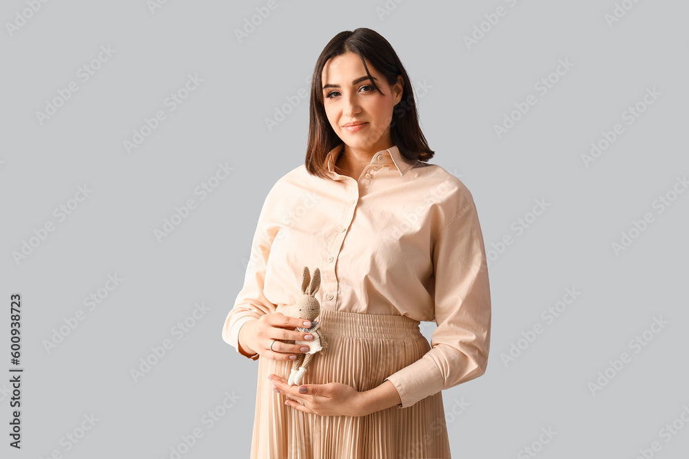 Young pregnant woman with baby toy on light background