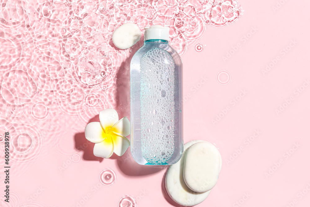 Bottle of micellar water with spa stones and plumeria flower in water on pink background