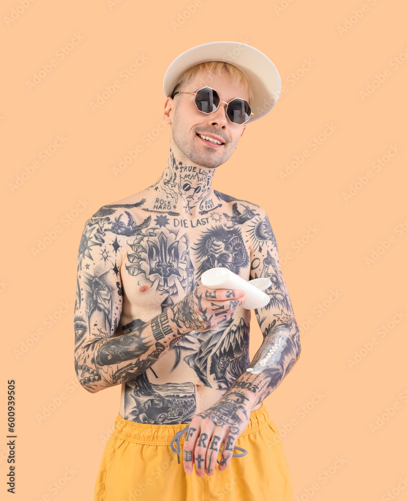 Tattooed man applying sunscreen cream on beige background