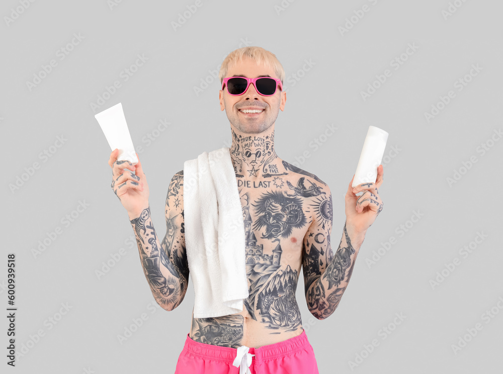 Tattooed man with sunscreen creams on light background