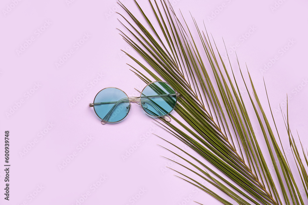 Round sunglasses with palm leaf on lilac background