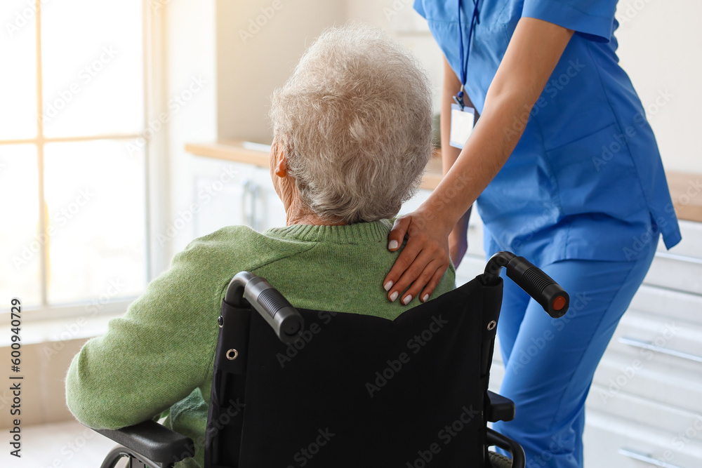 Young caregiver with senior woman in wheelchair at home, closeup