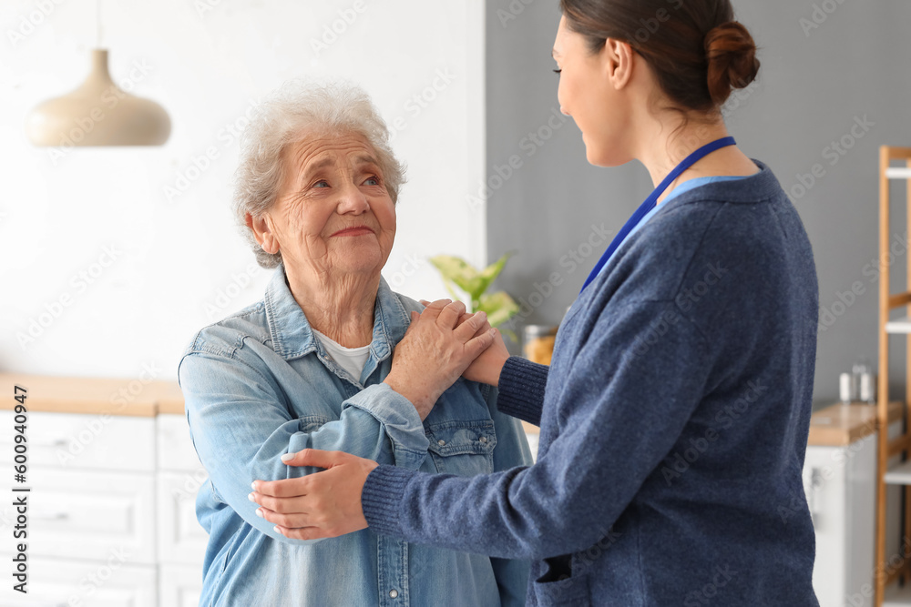 Young caregiver with senior woman hugging in kitchen