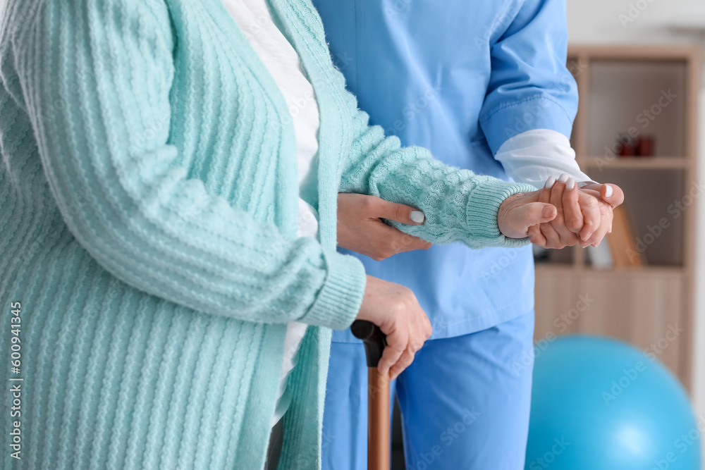 Young caregiver helping senior woman with walking stick at home, closeup