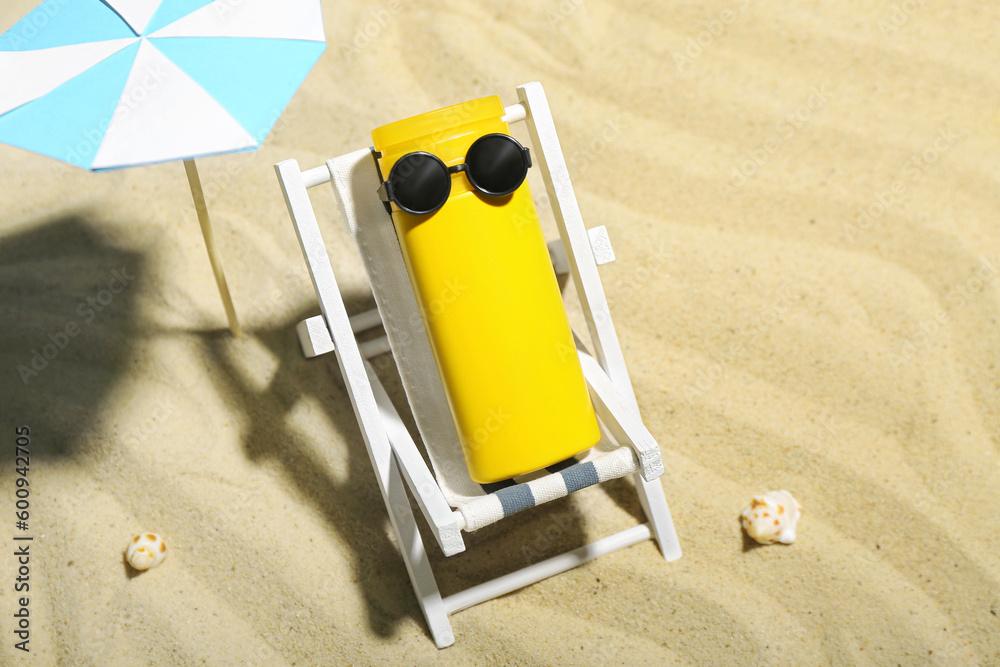 Creative composition with miniature deckchair, umbrella and sunscreen on sand