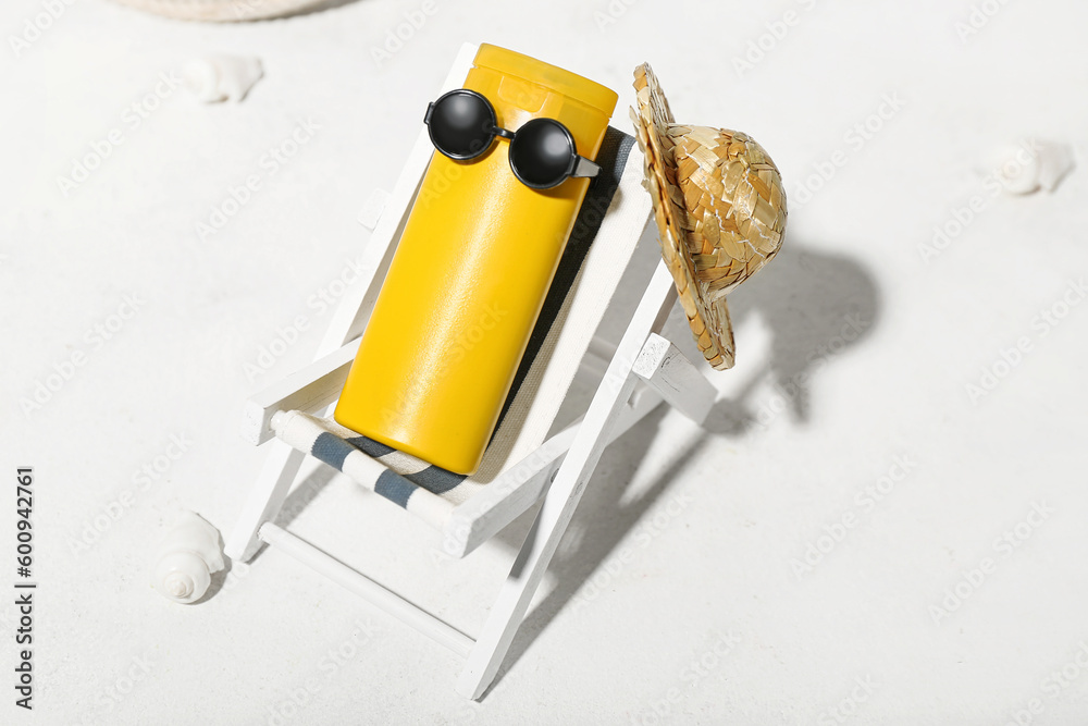 Creative composition with miniature deckchair and sunscreen on white background