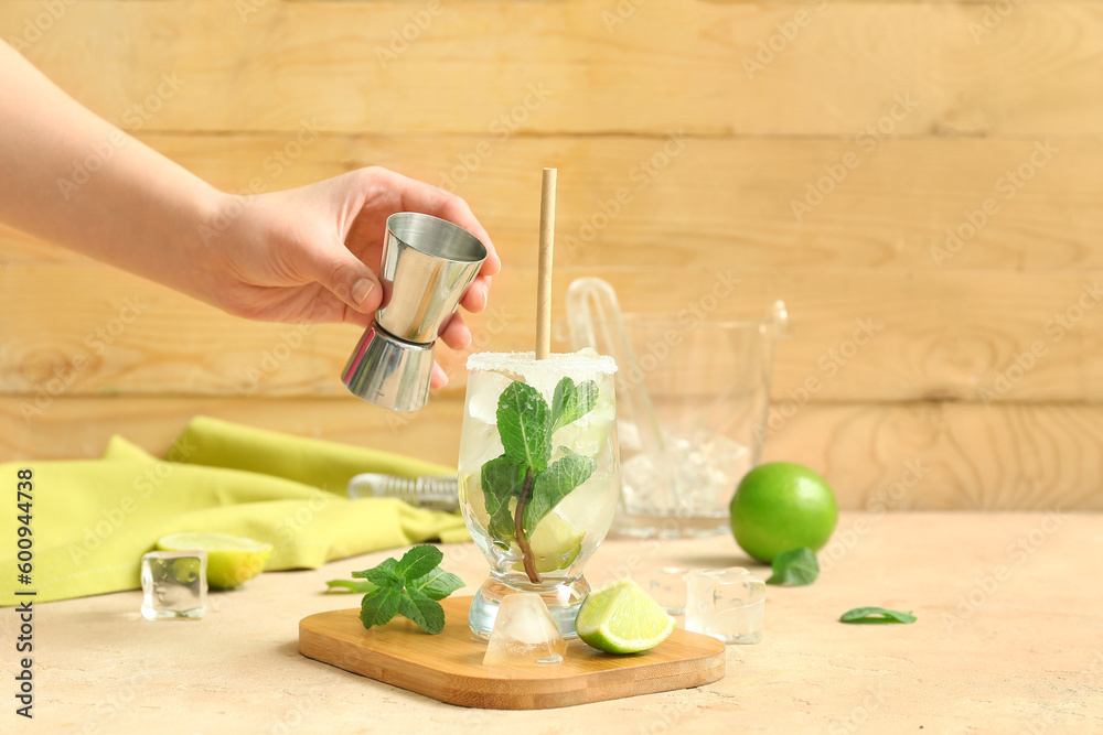 Female bartender making tasty mojito cocktail on table near wooden wall