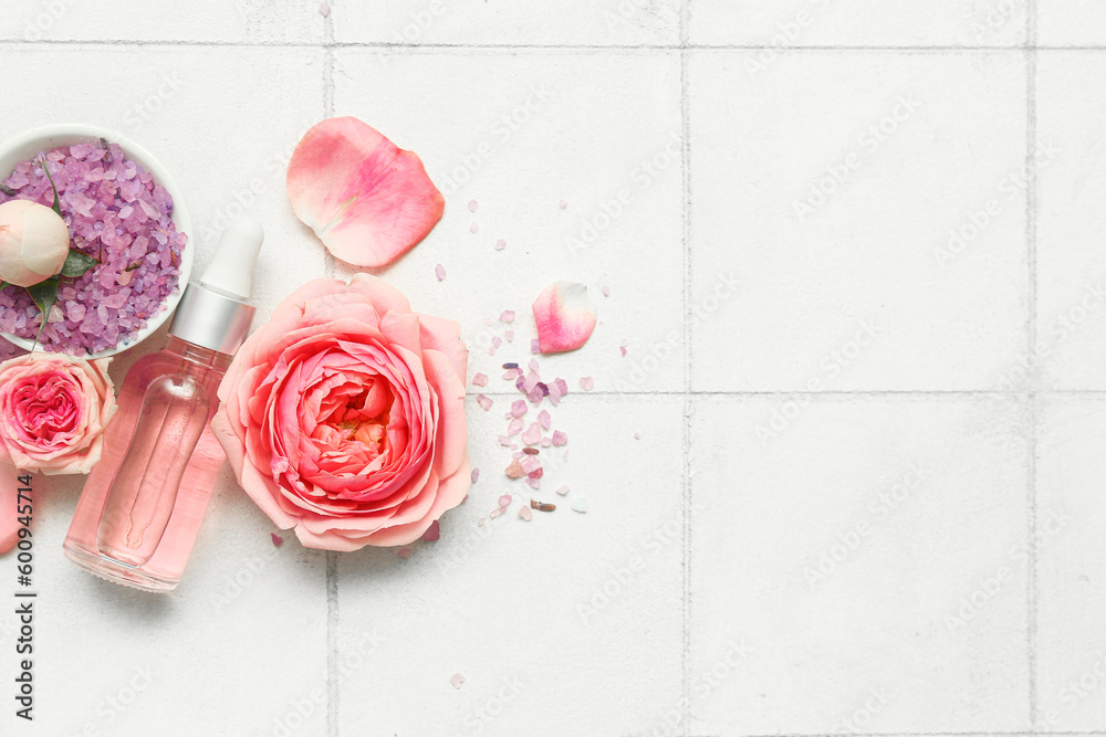 Bottle of cosmetic oil with rose extract and flowers on white tile background