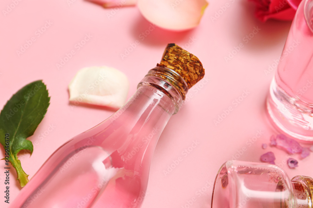 Bottles of cosmetic oil with rose extract on pink background, closeup