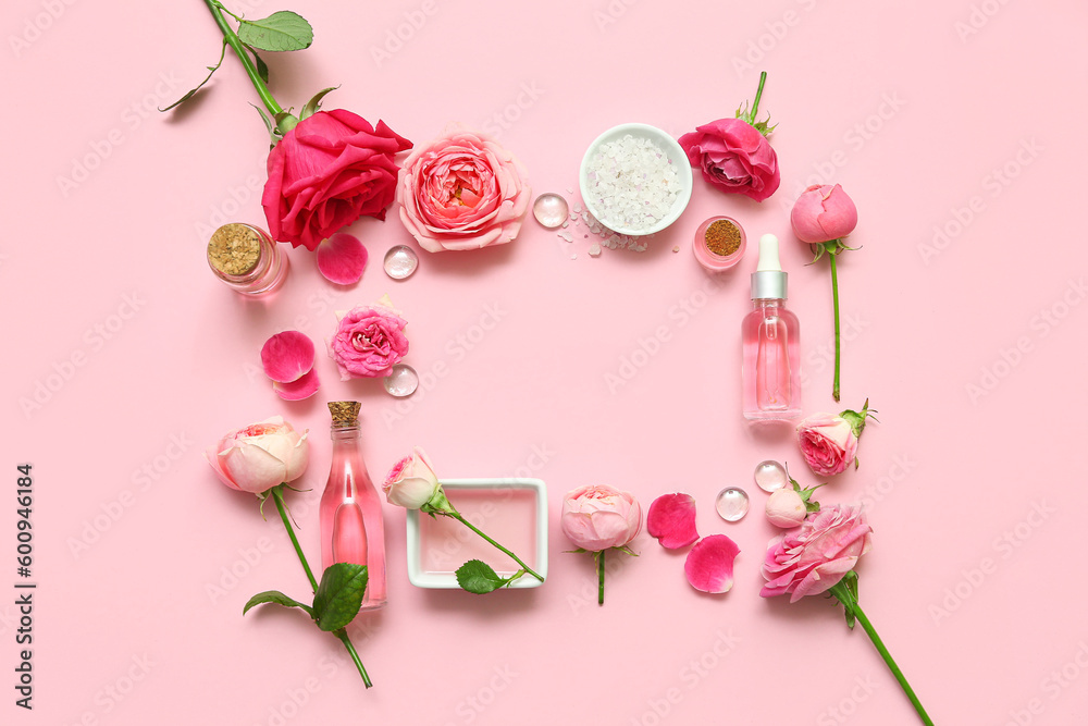 Frame made with bottles of cosmetic oil, rose flowers and salt on pink background