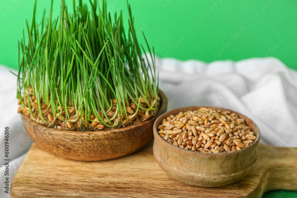 Bowl with fresh wheatgrass and wooden board on green background