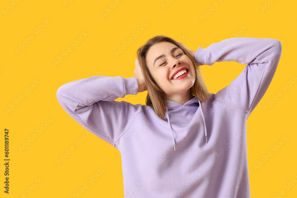 Happy young woman in lilac hoodie on yellow background