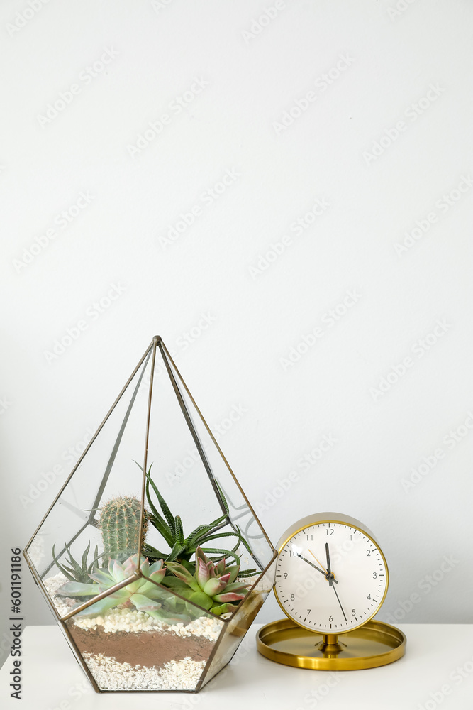 Florarium with alarm clock on table in light bedroom