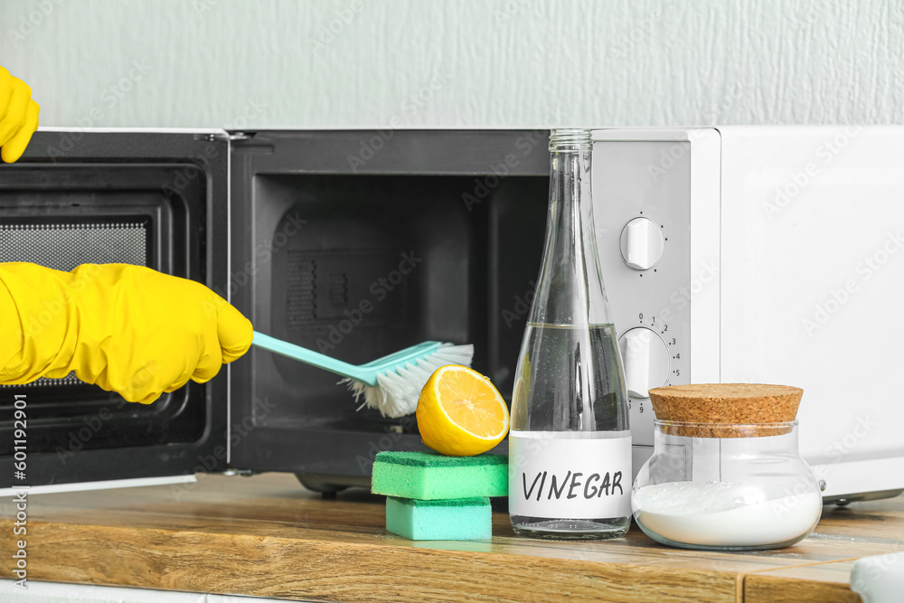 Woman cleaning microwave oven with brush, baking, soda and vinegar at home