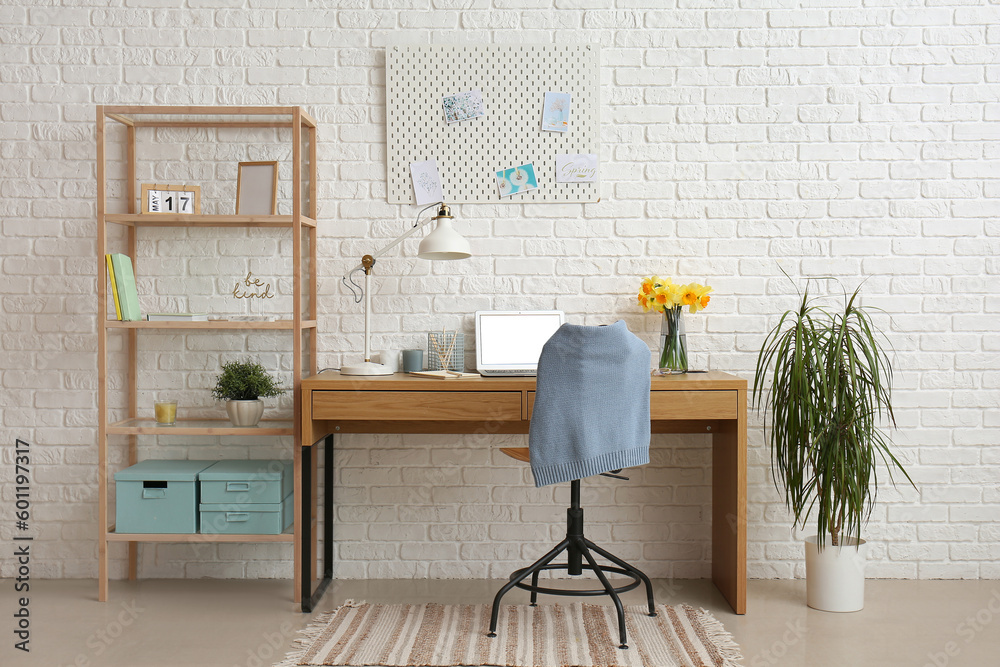 Workplace with modern laptop and shelving unit near white brick wall