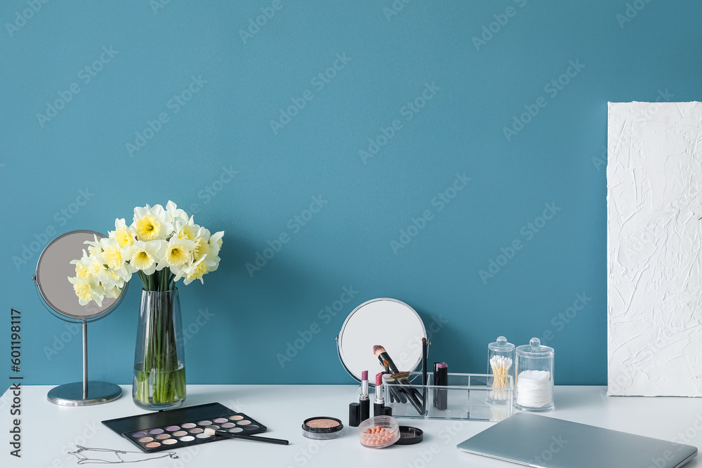 Table with different cosmetics and narcissus flowers near blue wall