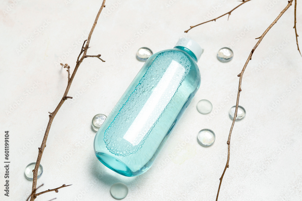 Bottle of micellar water with tree branches and glass stones on light background, closeup