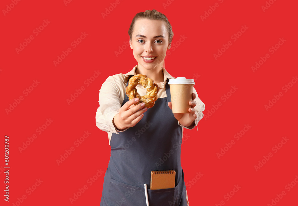 Young barista with cup of coffee and bun on red background