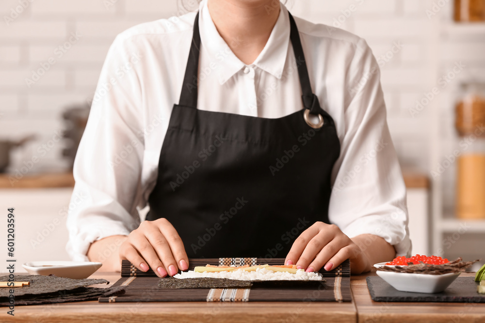 Woman preparing delicious sushi rolls in kitchen