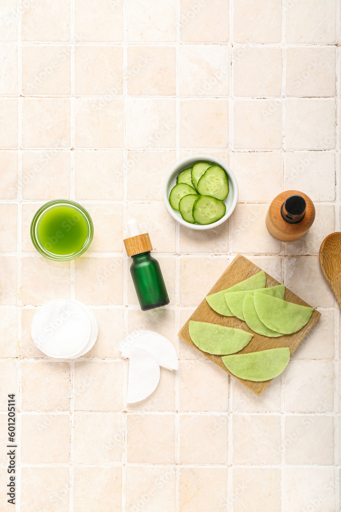 Cotton under-eye patches made with cucumber and materials on light tile background