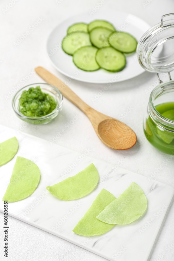 Cotton under-eye patches with cucumber slices on white table