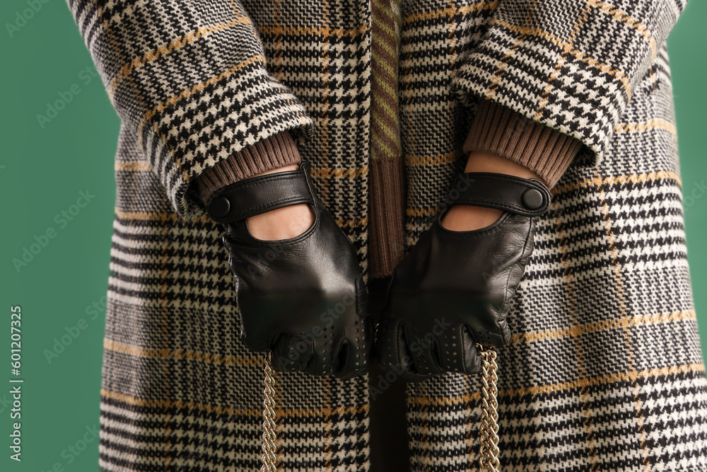 Beautiful young woman in leather gloves and coat on green background, closeup