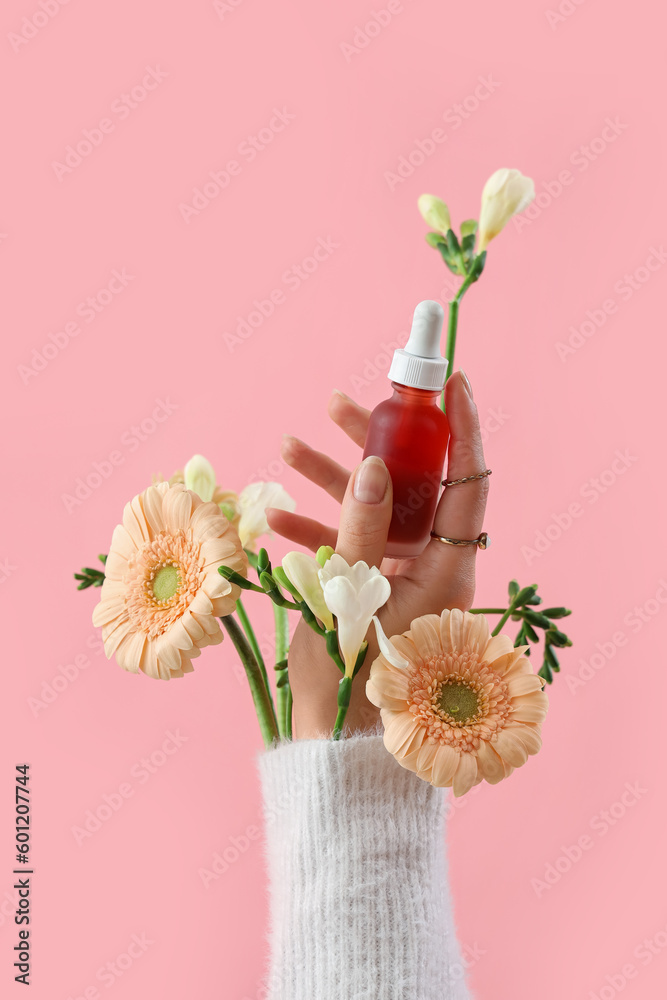 Hand holding cosmetic product and flowers on pink background