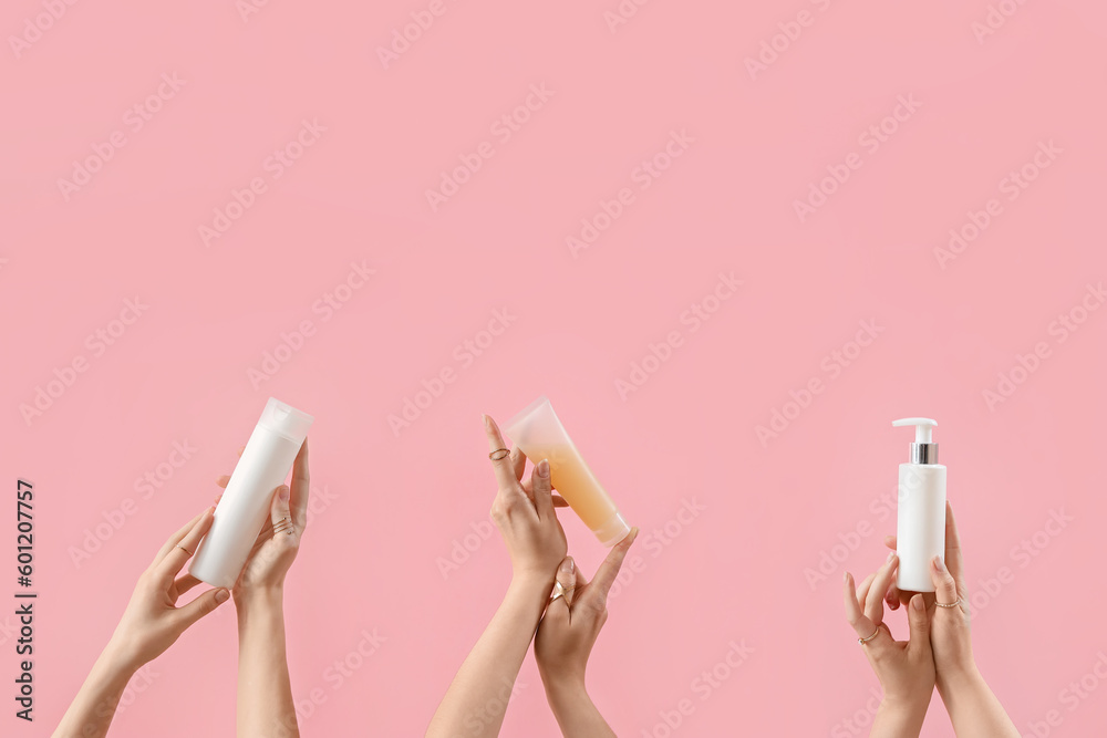 Hands holding cosmetic products on pink background