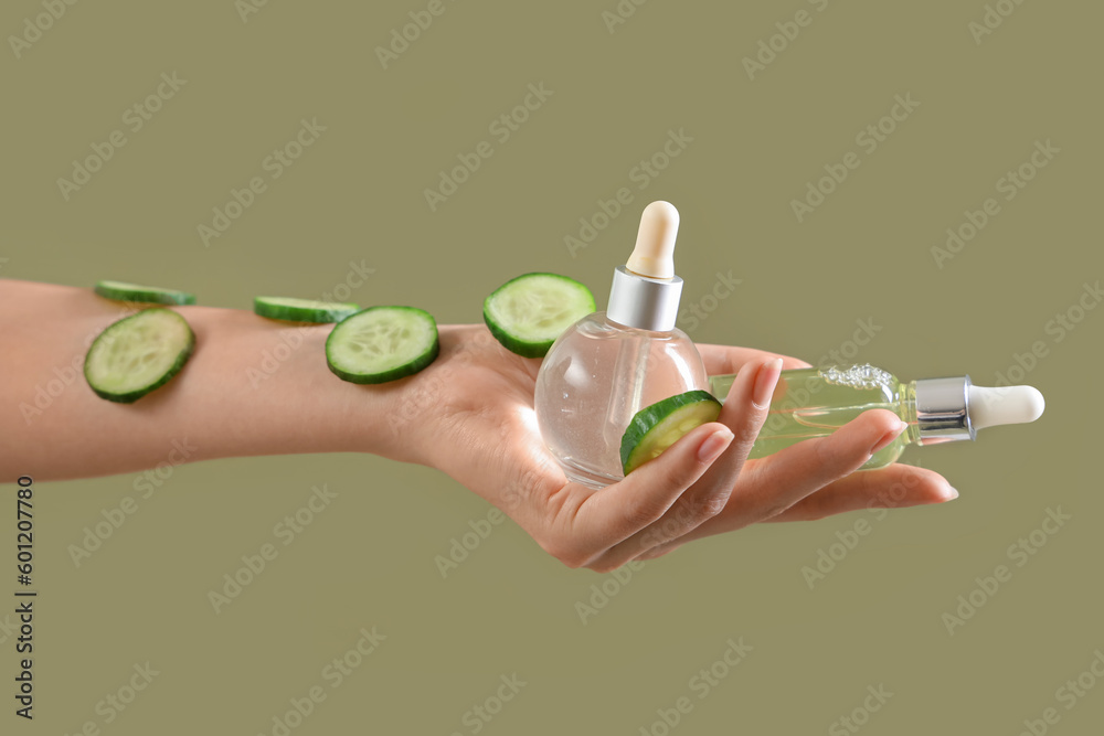 Hand holding cosmetic product and cucumber slices on color background