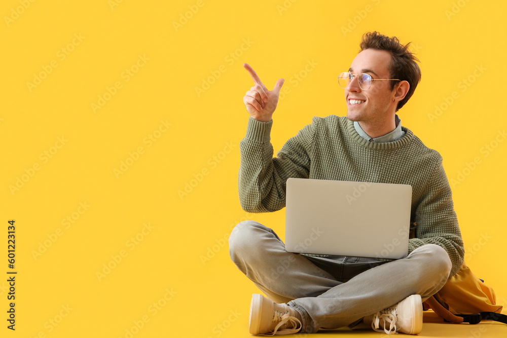 Male student with laptop pointing at something on yellow background