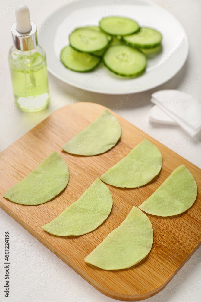 Board with cotton under-eye patches and cucumber slices on white background, closeup