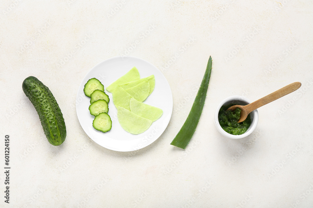 Plate with cotton under-eye patches, cucumber slices and aloe leaf on white background