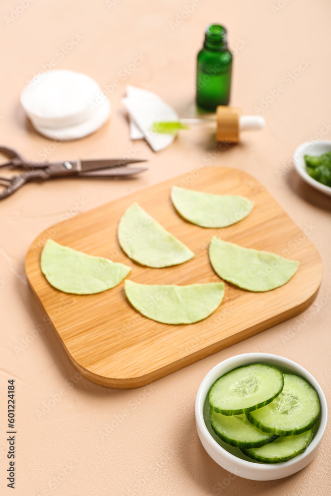 Board with cotton under-eye patches and cucumber slices on beige background, closeup