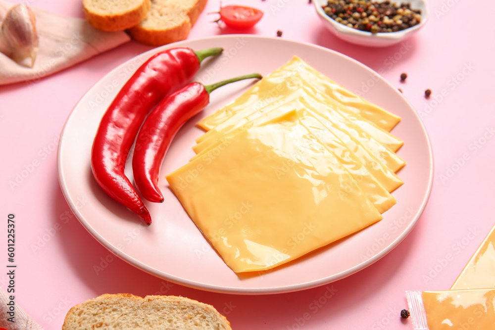 Plate of tasty processed cheese with bread and chilli on pink background