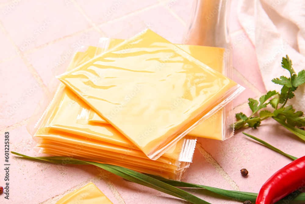 Slices of tasty processed cheese with scallions and chilli on pink tile background