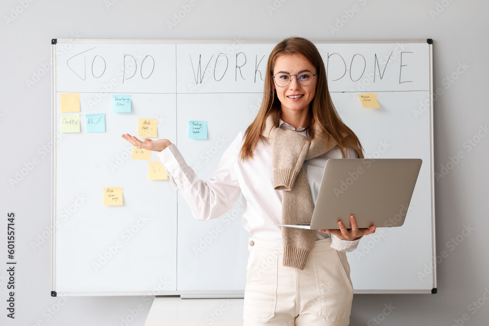 Young businesswoman with laptop near scrum task board in office